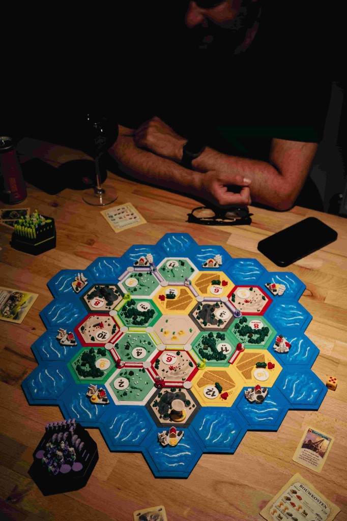 Friends playing a game of Catan around a table at a board game night